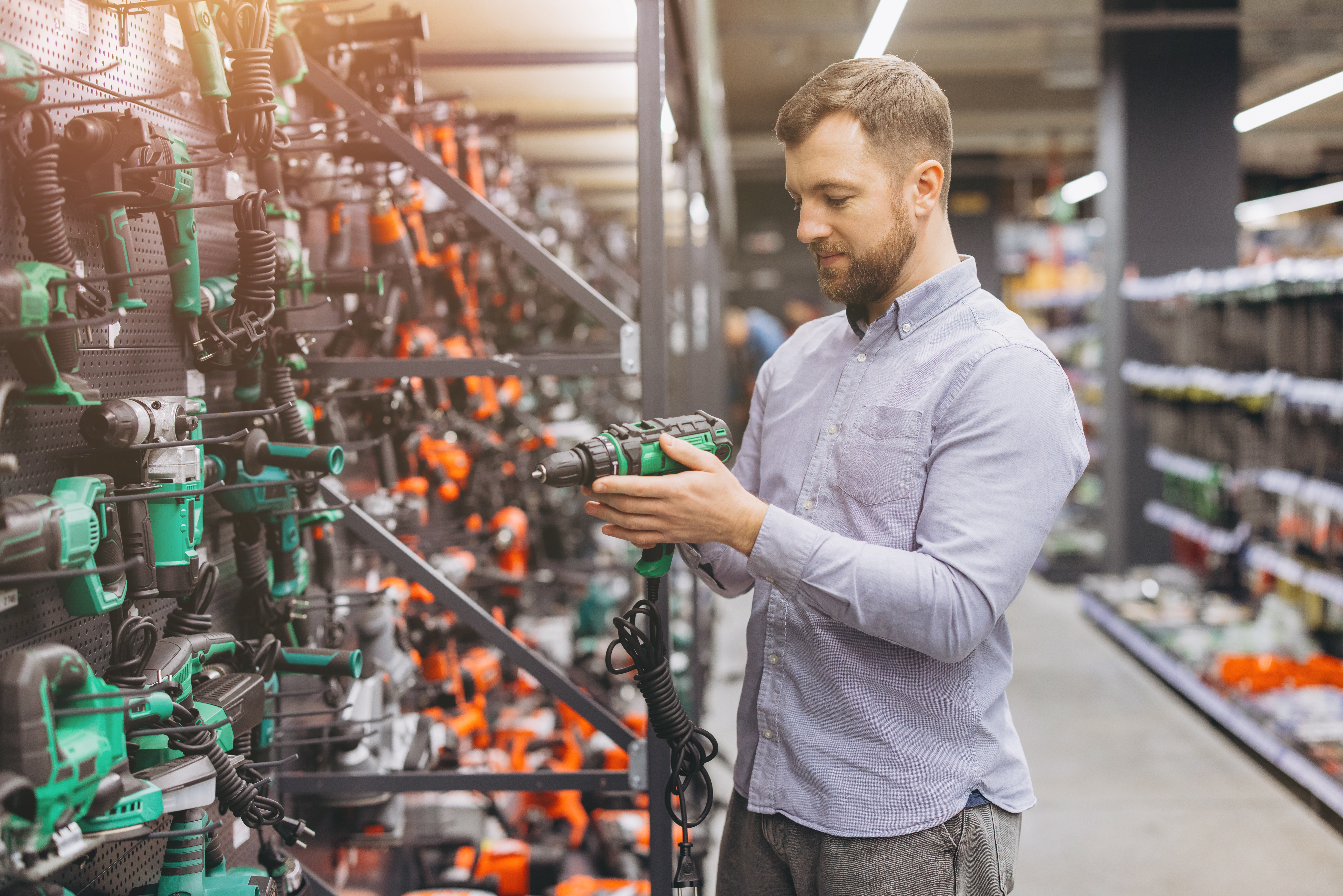 Man examining a power drill in a hardware store, focusing on different models for construction and DIY projects